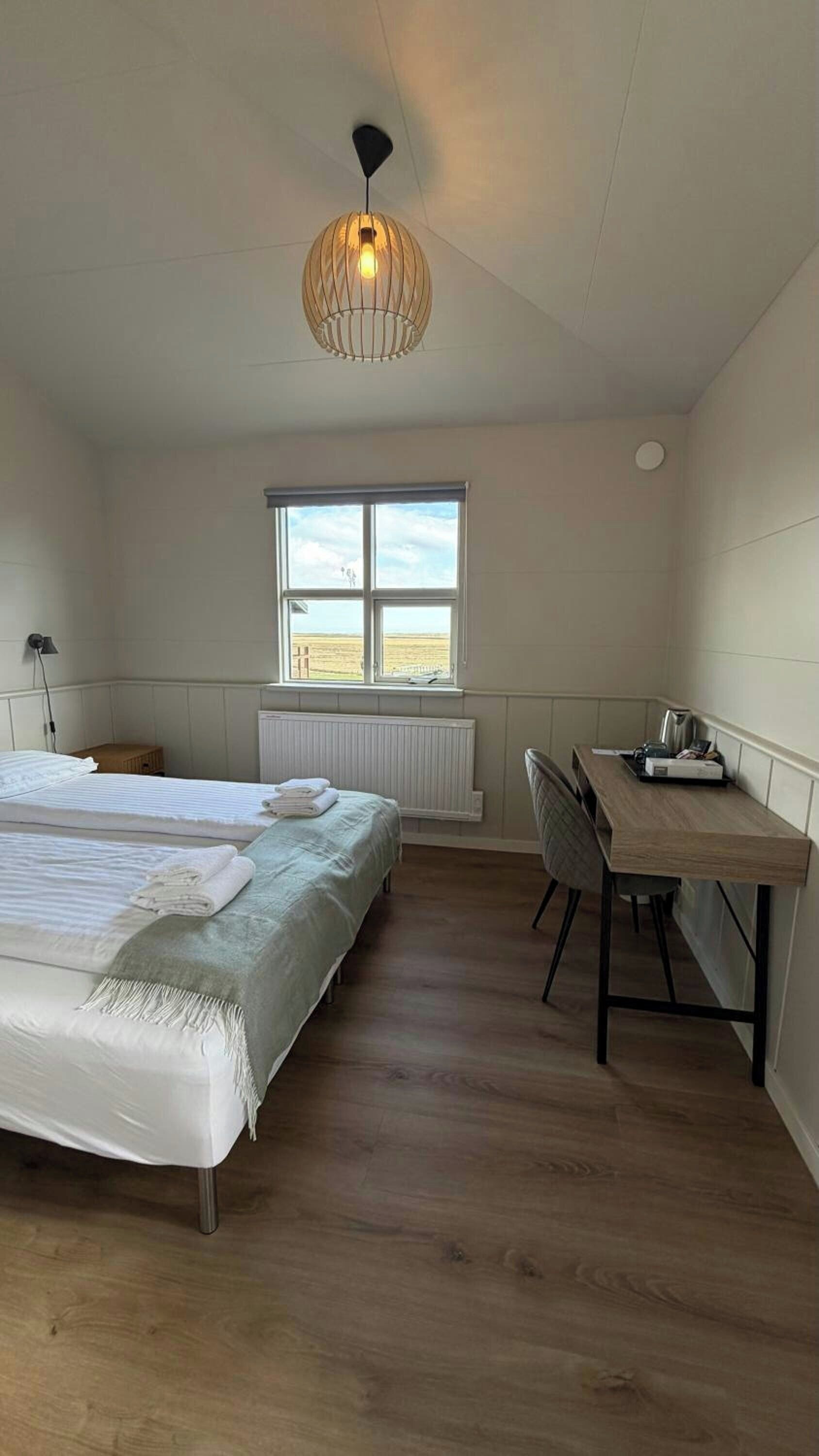 Ein Schlafzimmer mit Bett, Schreibtisch, Stuhl, Heizkörper und einem Fenster mit Blick.