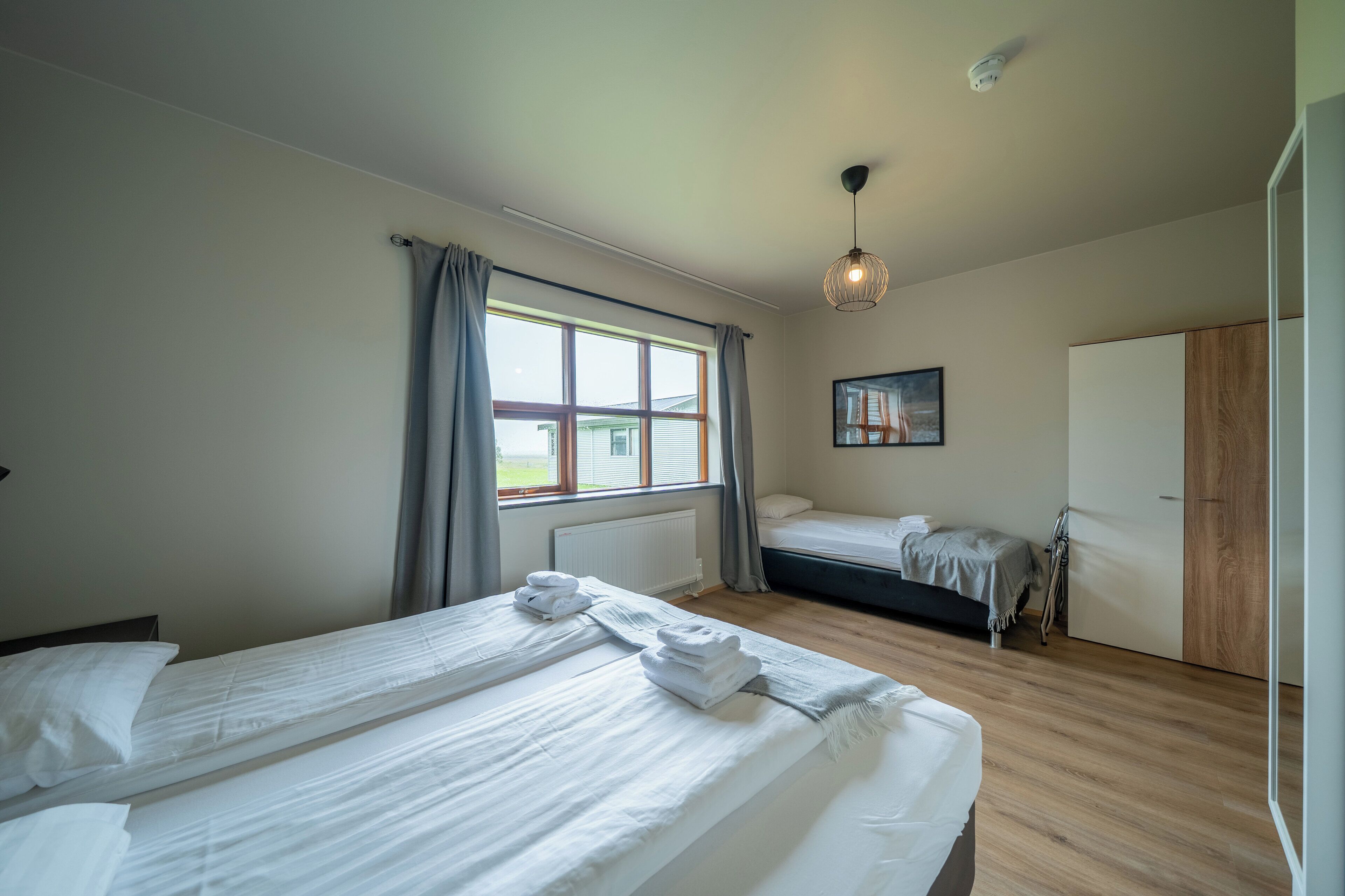 Un dormitorio con una cama grande, una cama más pequeña, una ventana con cortinas, un cuadro en la pared y un armario.
