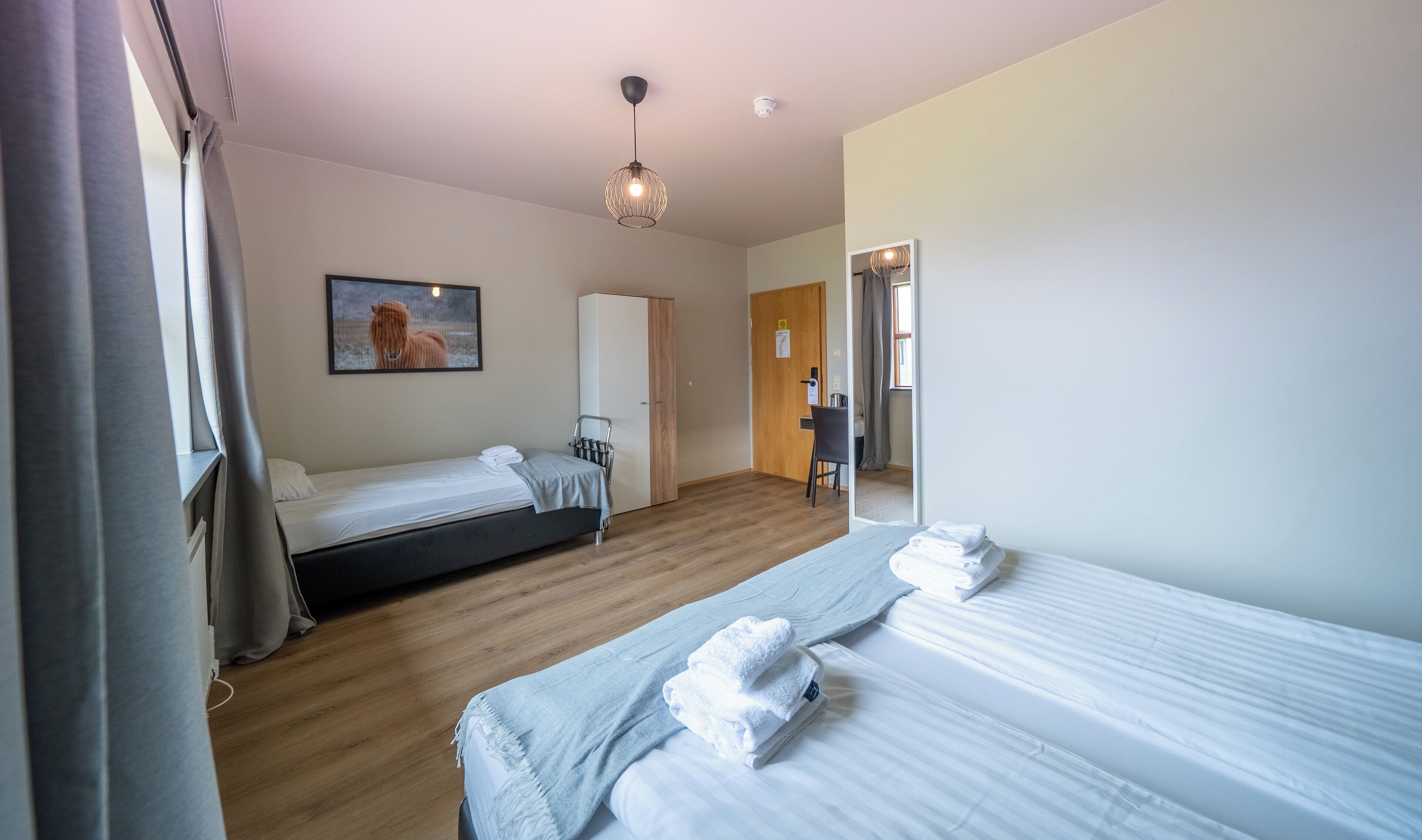 Ein Hotelzimmer mit zwei Betten, Holzboden, einem Gemälde von einem Pferd, einem Kleiderschrank und einem Schreibtisch mit Stuhl.