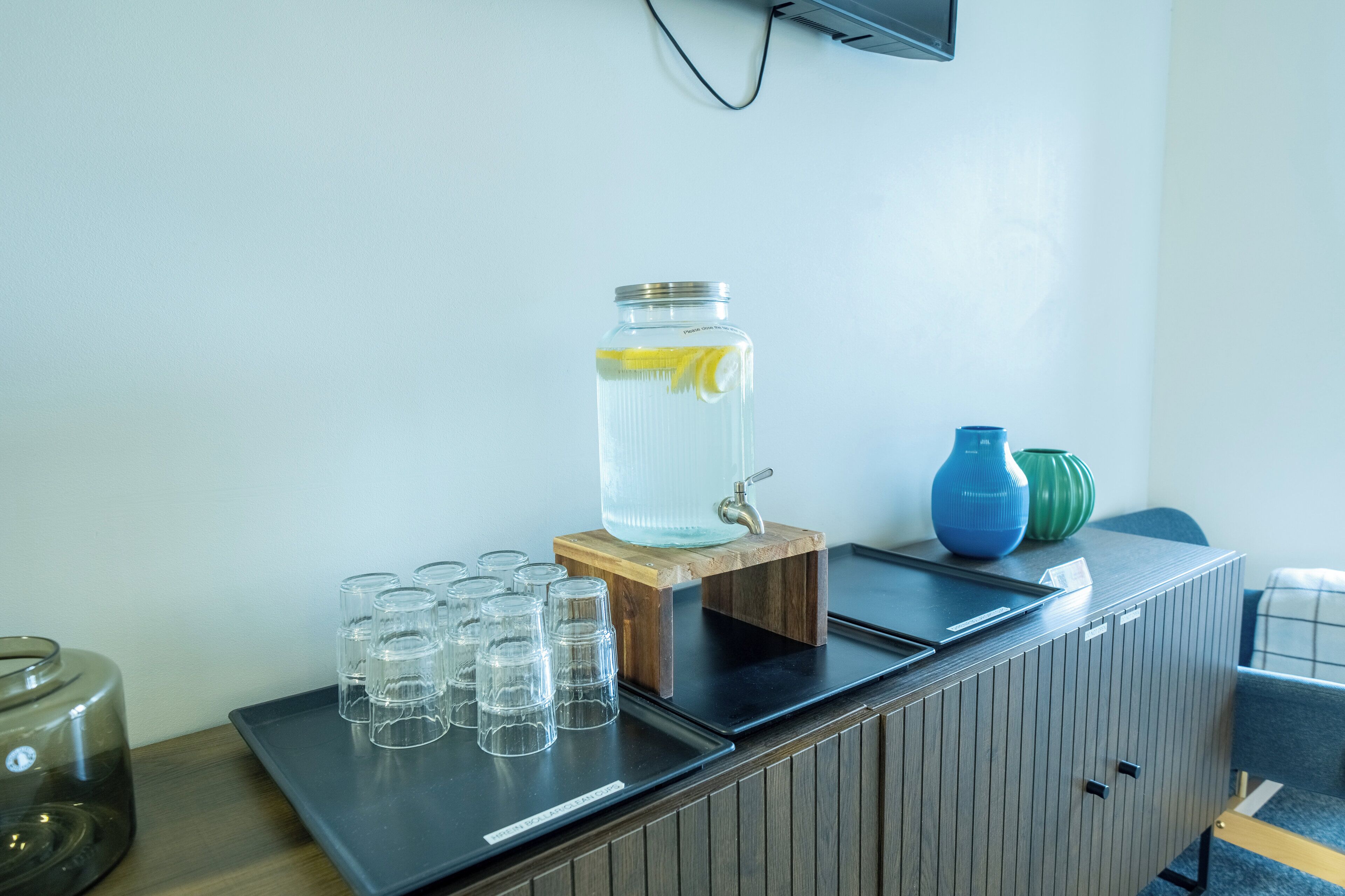 A water dispenser with a lemon slice, glasses, and decorative vases on a counter.