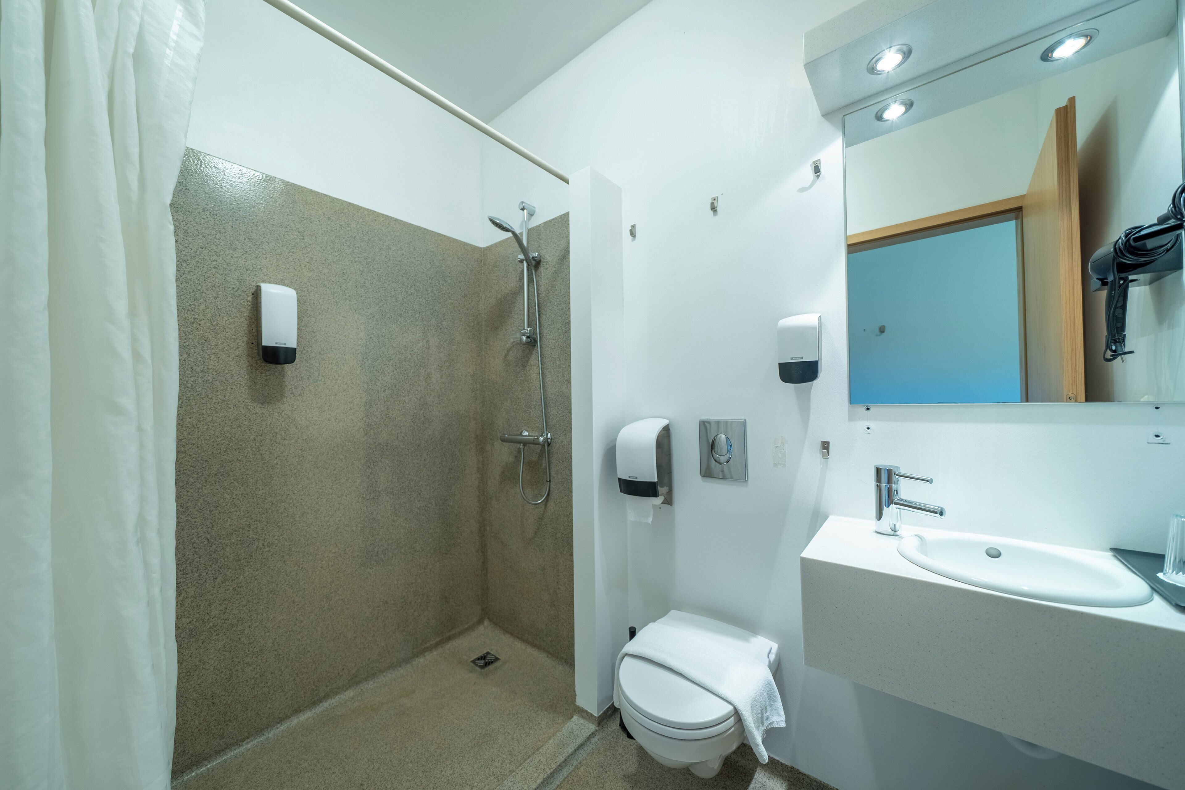 Un baño moderno con ducha, inodoro, lavabo y secamanos.
