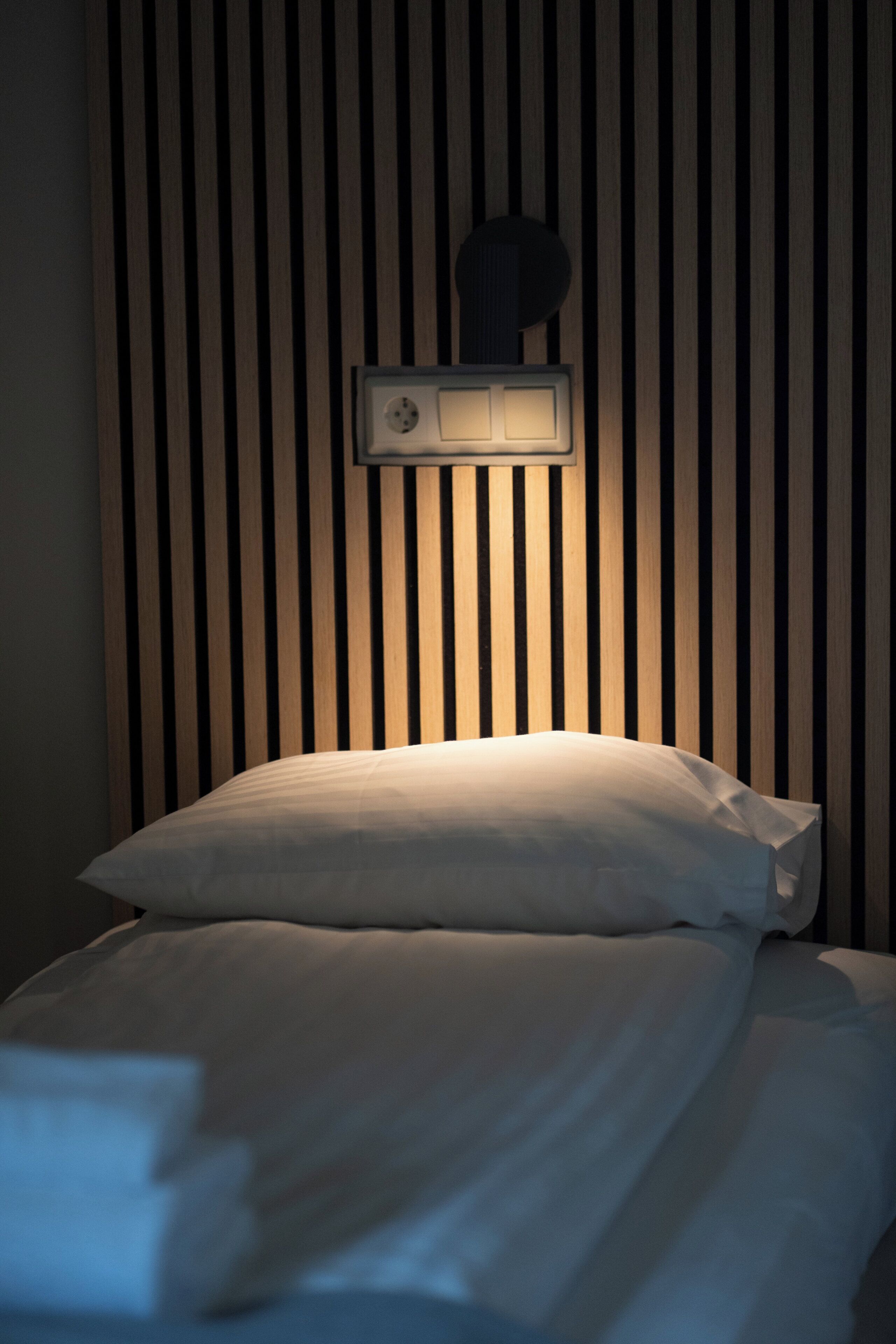 A neatly made bed with a white pillow and a headboard with vertical wooden slats.