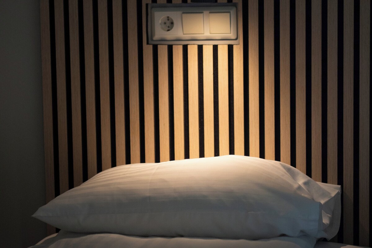 Cama bem arrumada com travesseiro branco e cabeceira de ripas verticais de madeira.