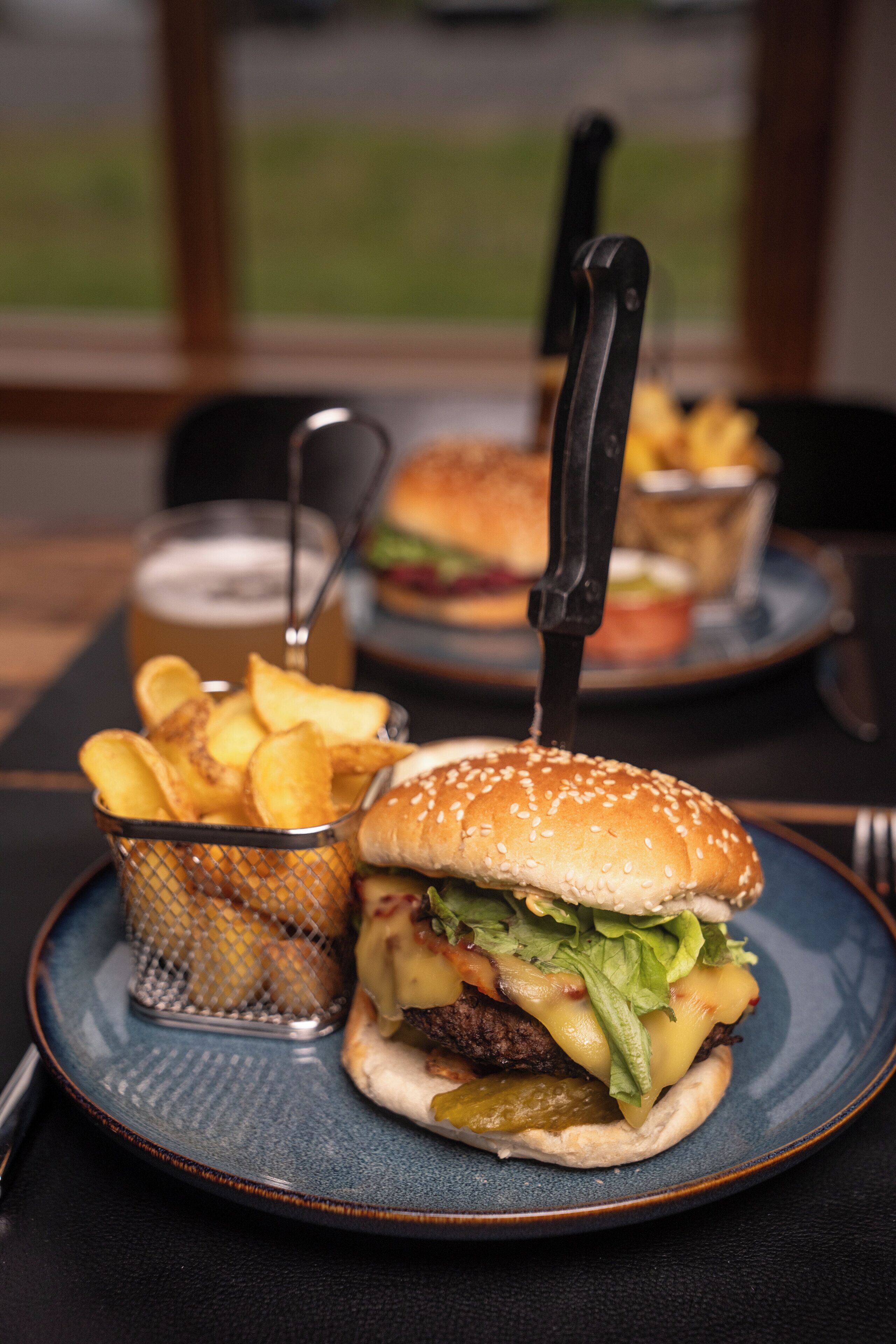 Ein Teller mit einem Burger, Pommes und einem Getränk auf einem Tisch.
