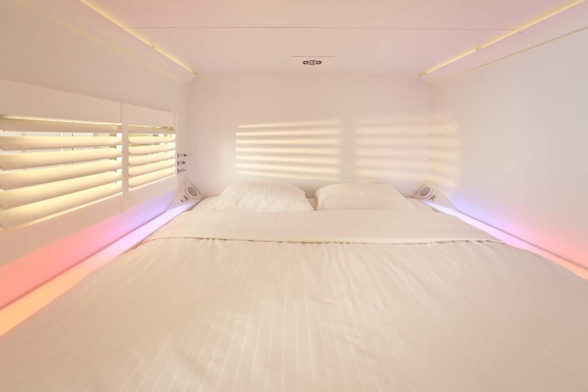 Une chambre à coucher avec un lit, une fenêtre avec des stores et un luminaire au plafond.