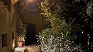 A narrow stone pathway leading to a building entrance, flanked by potted plants and illuminated by a street lamp. - The colors of Chianti  (Mercatale In Val di Pesa)