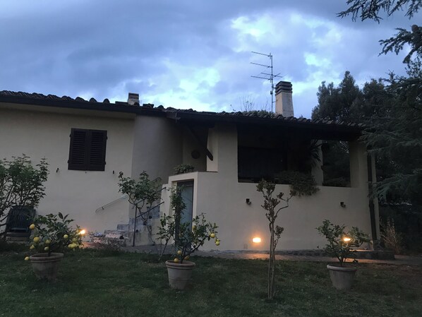 A house with a tiled roof, a chimney, and a small porch area. There are potted plants in the front yard.