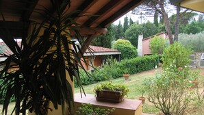 A covered patio area with potted plants and a view of a garden and buildings in the background. - The colors of Chianti  (Mercatale In Val di Pesa)