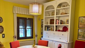 A dining area with a round table, red chairs, a white cabinet with shelves, and a window with curtains. - The colors of Chianti  (Mercatale In Val di Pesa)