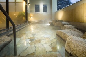 Un espace intérieur dallé de pierre, avec de gros rochers et un escalier.