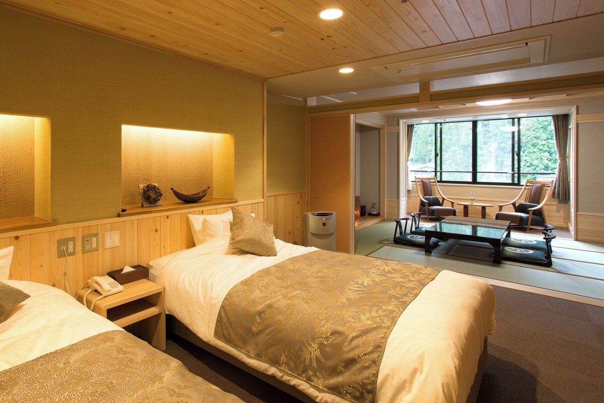 A hotel room with two beds, a sitting area with a table and chairs, and a view of the outdoors.