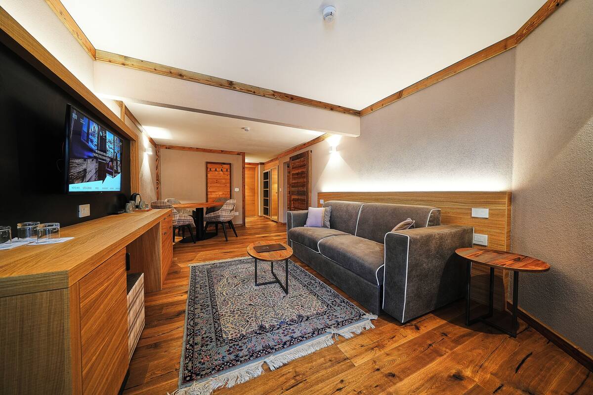 A modern living room with a wooden floor, a grey sofa, a small coffee table, and a TV mounted on the wall.