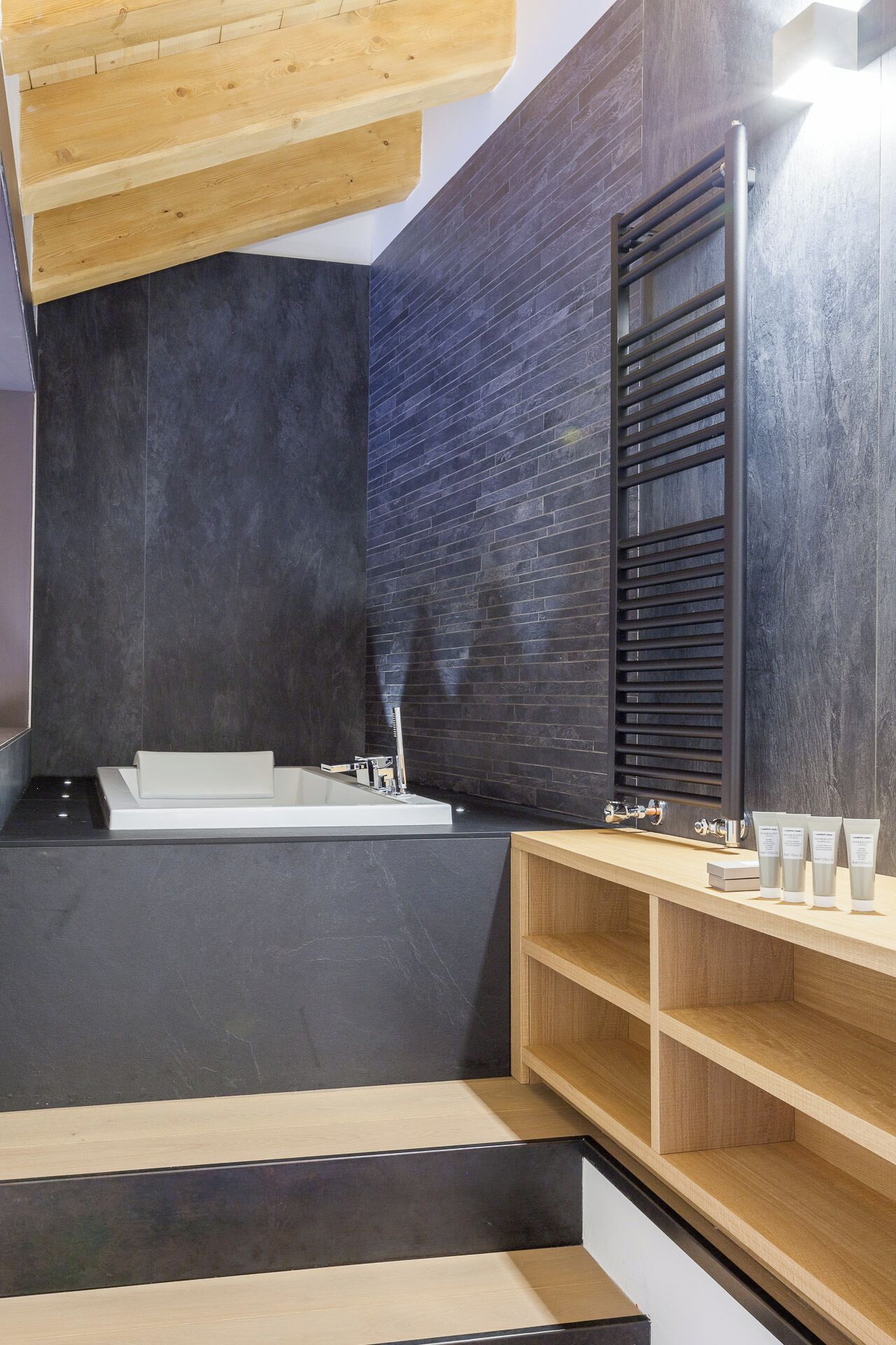 Une salle de bain moderne avec une grande baignoire, un meuble-lavabo en bois et un porte-serviettes noir.