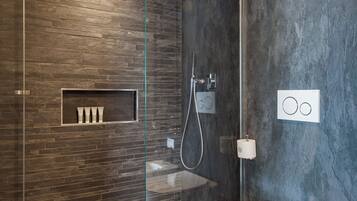 A modern bathroom with a glass-enclosed shower, a built-in shelf with toiletries, and a toilet with a bidet attachment.