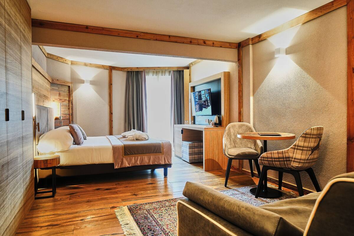 A cozy hotel room with a bed, a desk, two chairs, and a television.