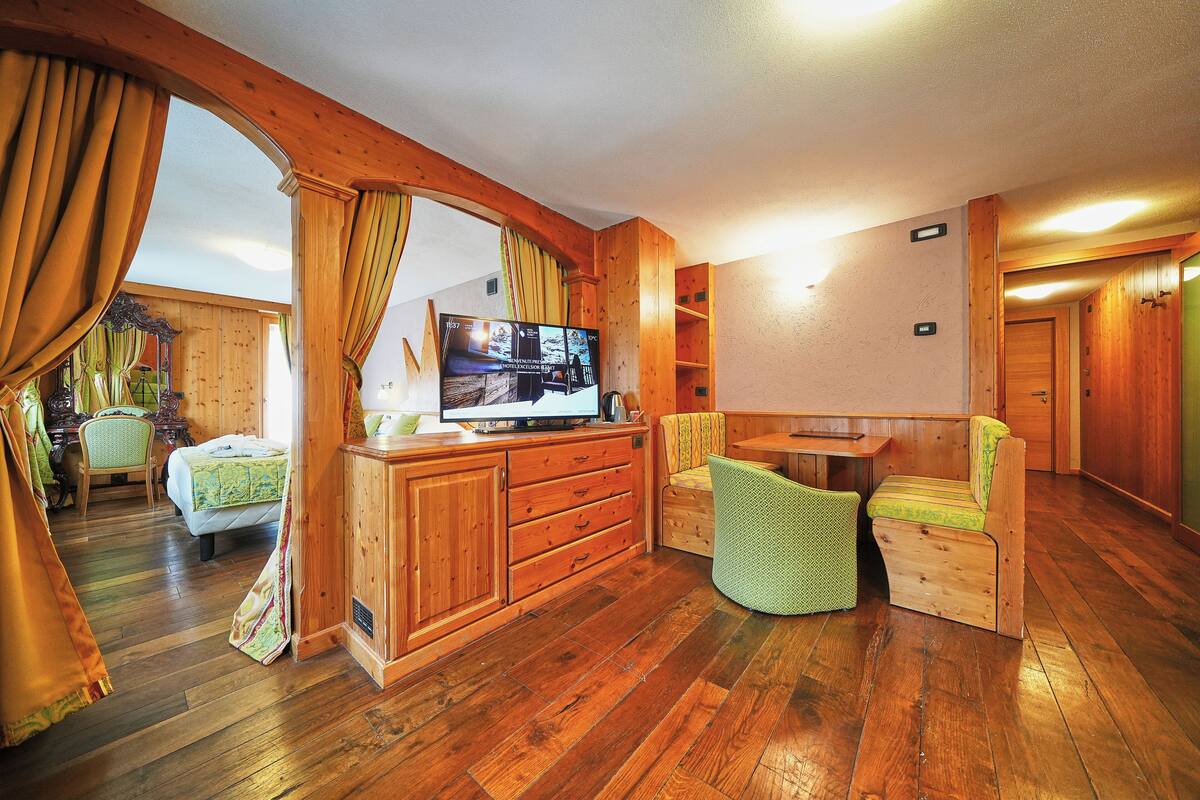 A wooden-floored room with a television, a bed, a desk, and a chair.