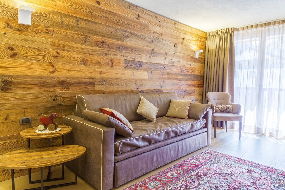 A modern living room with a wooden wall, a sofa, a chair, and a small round table with a decorative item.