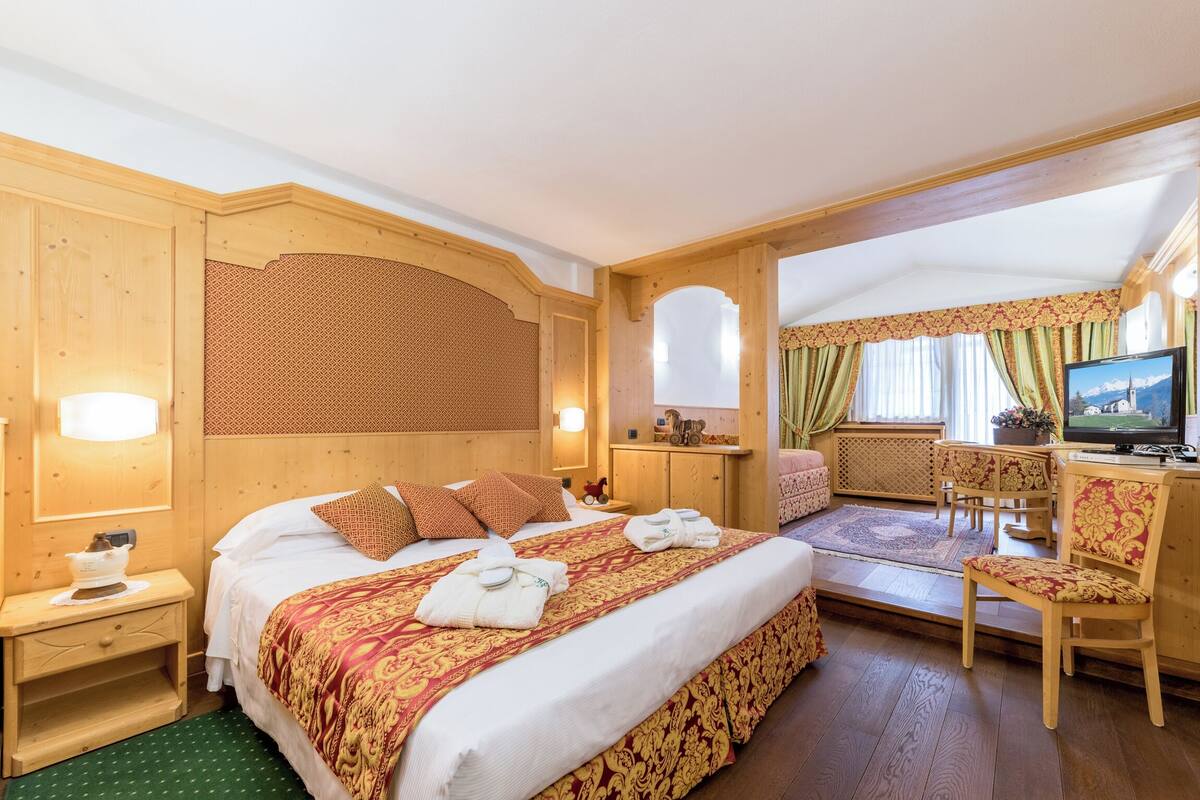 A hotel room with a large bed, a desk with a chair, a television, and a window with curtains.