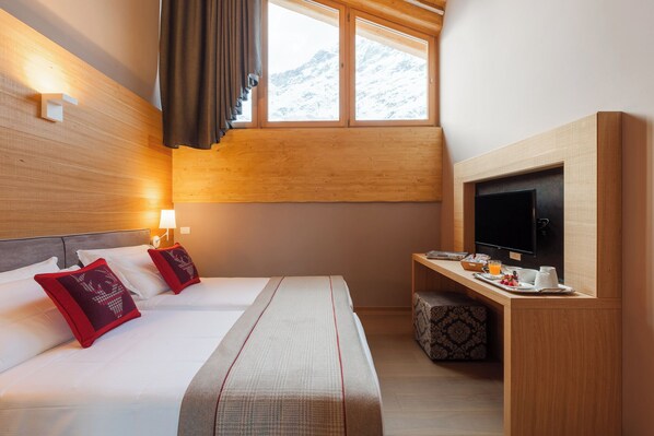 Une chambre d’hôtel avec un lit, un bureau avec une télévision et une fenêtre donnant sur la montagne.