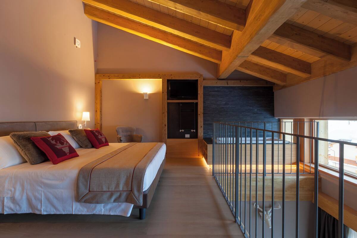 A bedroom with a large bed, a chair, a TV, and a balcony with a railing.