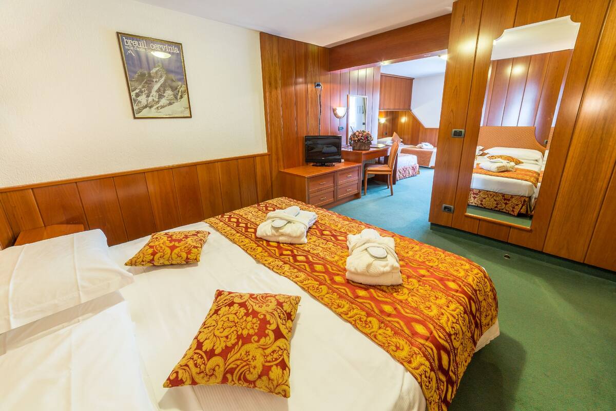 A hotel room with a large bed, a desk, a television, and a mirror.