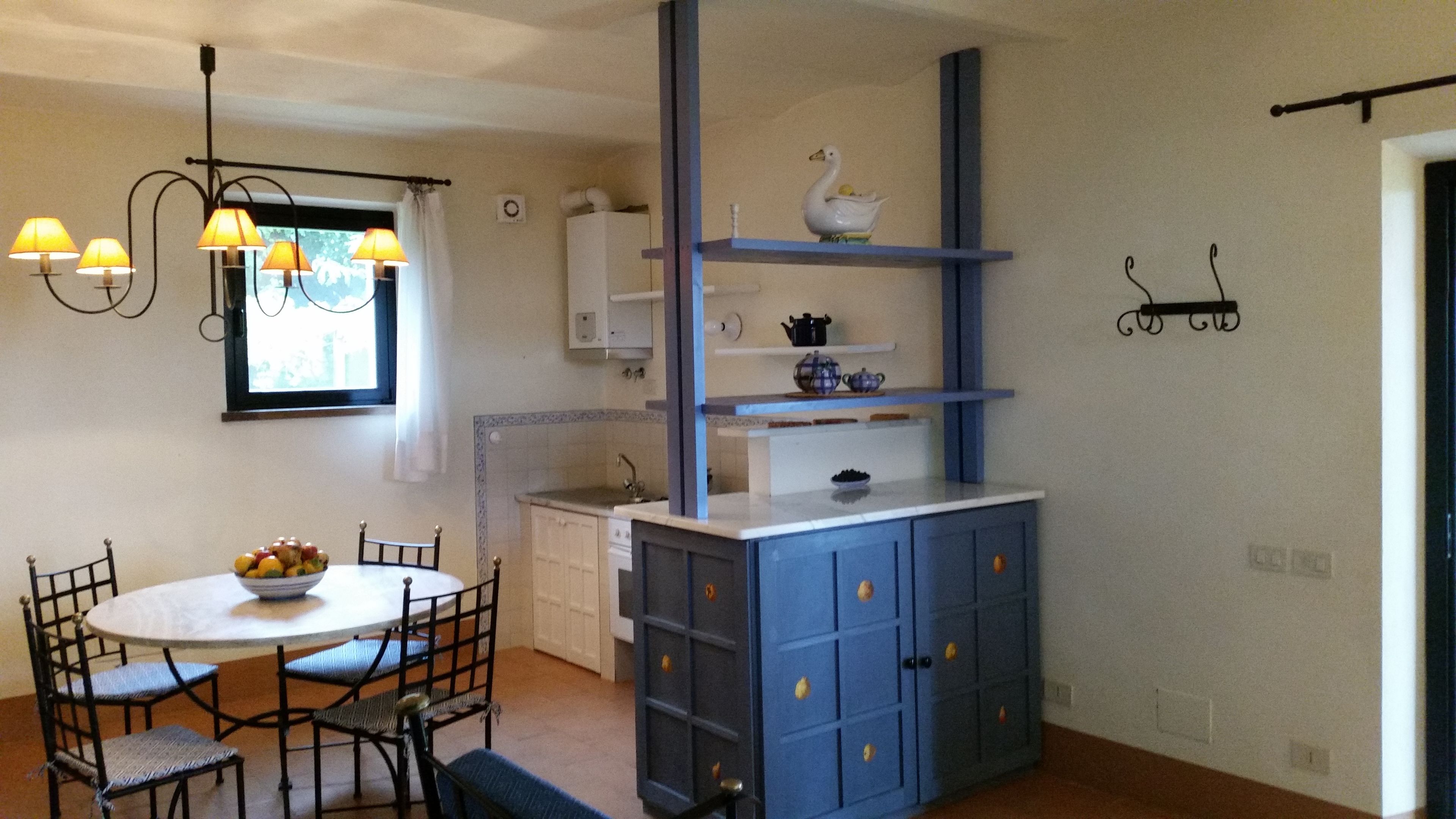 A kitchen with a blue cabinet, a dining table with chairs, and a window with curtains.