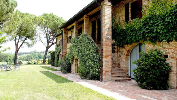 A rustic building with a brick exterior, ivy-covered walls, and a paved pathway leading to a seating area with chairs. - Agriturismo Poggio alle Vigne (Torgiano)