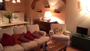 A cozy living room with a sofa, armchair, wooden coffee table, and a television on a stand. - Agriturismo Poggio alle Vigne (Torgiano)