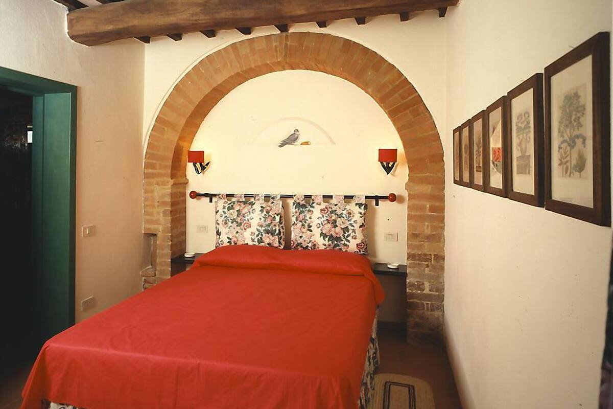 Une chambre à coucher avec un lit, un mur en briques en arc de cercle, un plafond en bois et des tableaux encadrés accrochés au mur.