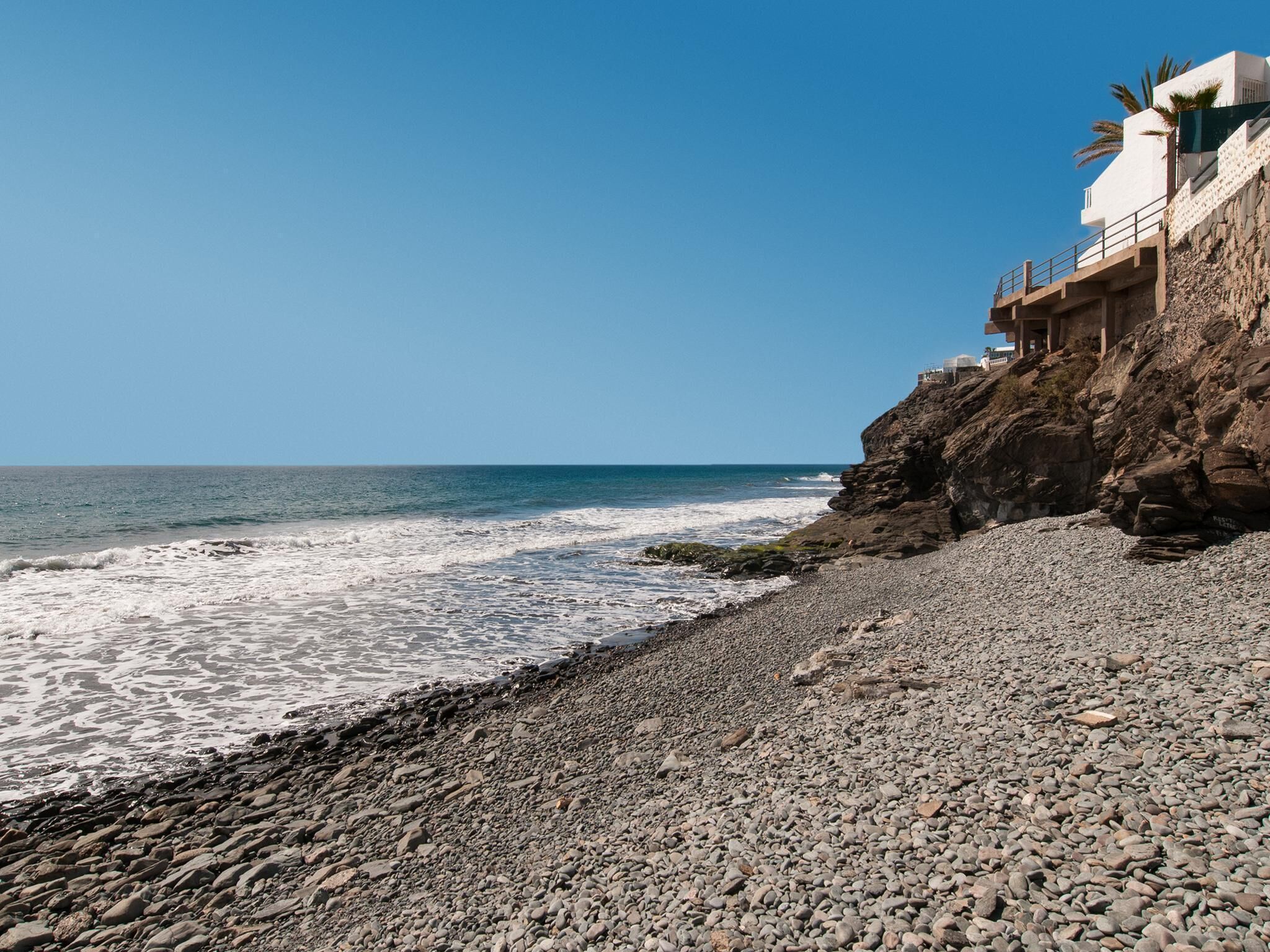 Una playa rocosa con un edificio en un acantilado con vistas al océano.