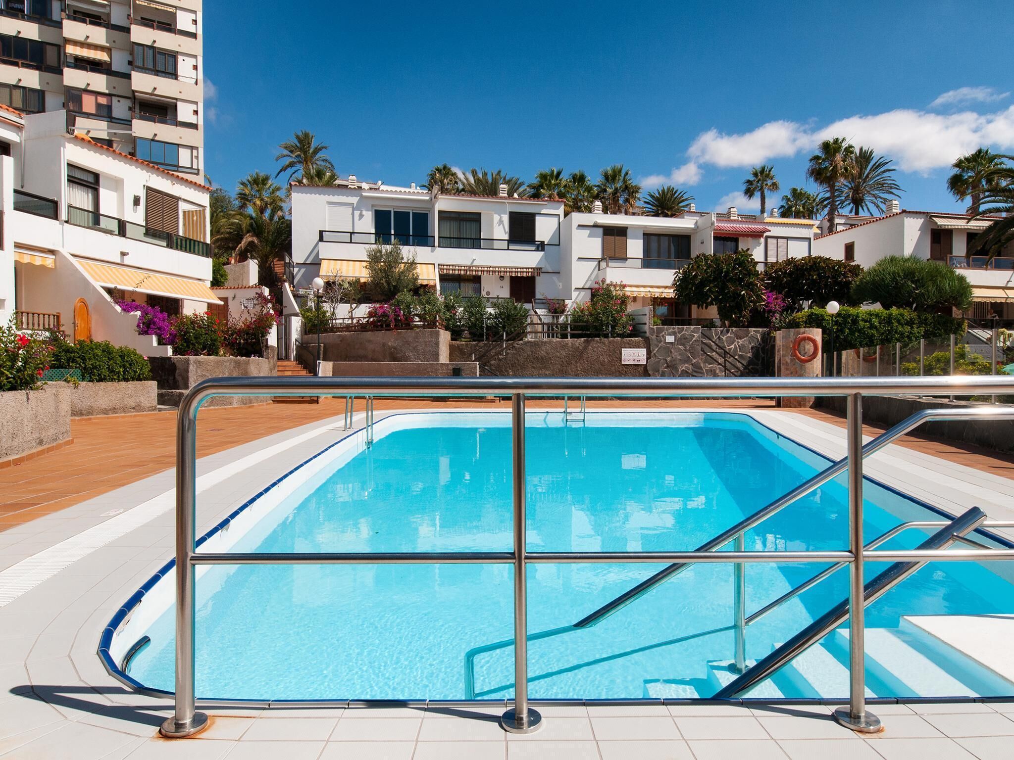 A swimming pool with a metal railing, surrounded by a tiled deck.