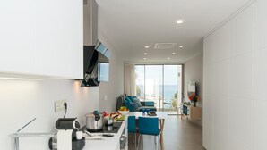 Una cucina moderna con mobili bianchi, una cappa aspirante nera e un'area pranzo con sedie blu e un tavolo.