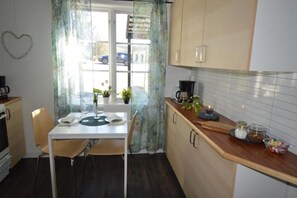 Una cocina compacta con una mesa de comedor, sillas, cafetera y una ventana con cortinas.