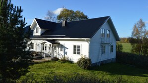 Une maison blanche à deux étages, avec un toit sombre, un porche à l’avant et un escalier bien visible menant à l’entrée.