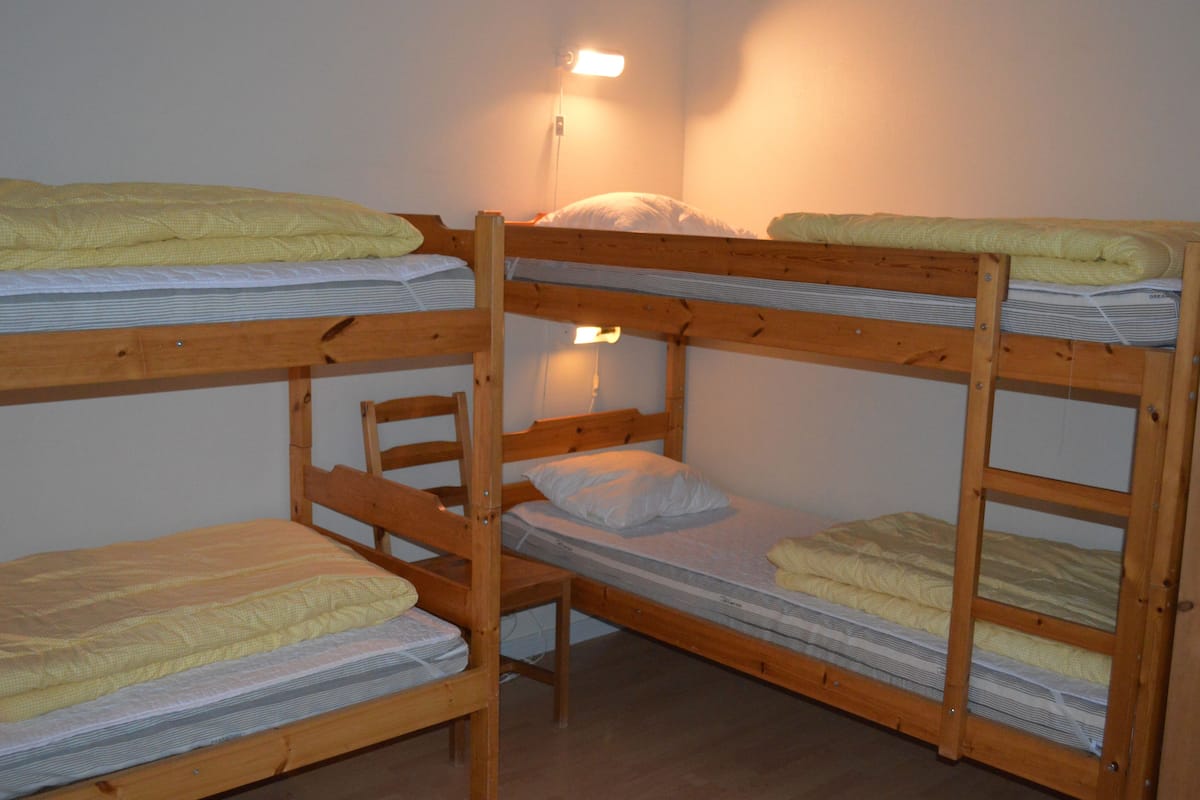 Une chambre avec un lit superposé en bois, une petite table de chevet et une lampe fixée au mur.