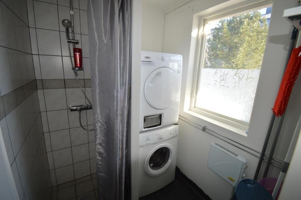 A small laundry room with a washing machine, a dryer, and a window with a view of trees.
