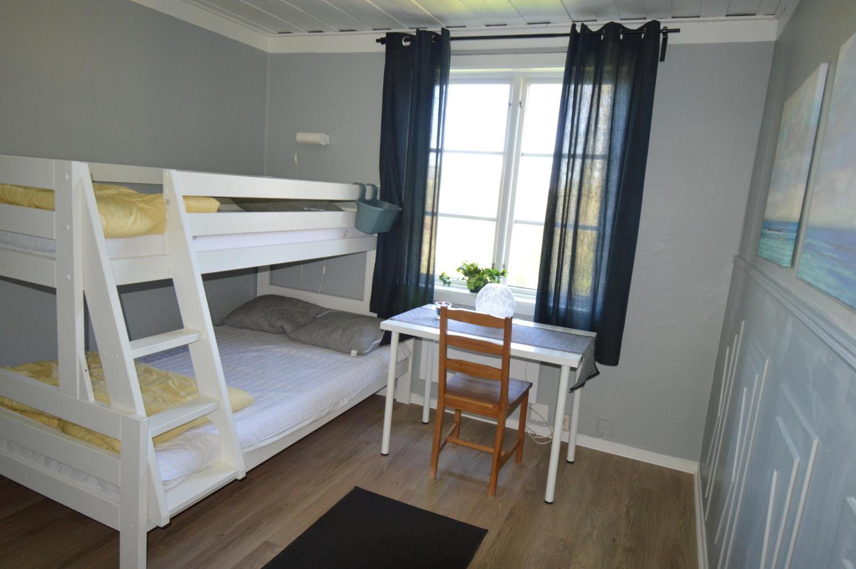 A bunk bed room with a desk and chair, a window with curtains, and a small plant on the windowsill.