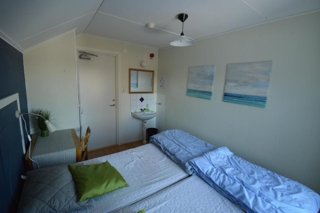 A bedroom with two beds, a bedside table, a mirror, a sink, and two wall-mounted paintings.