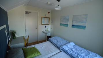 A bedroom with two beds, a bedside table, a mirror, a sink, and two wall-mounted paintings.