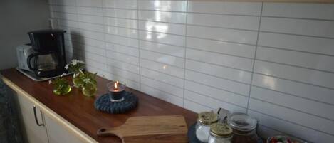 A kitchen counter with a coffee maker, a candle, jars, and a cutting board.