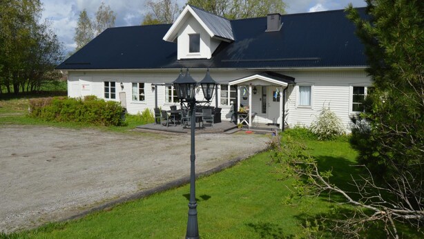 Un bâtiment blanc avec un toit foncé, une véranda et une allée gravillonnée.