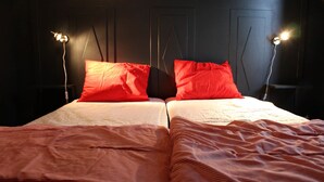 Un lit double avec des oreillers rouges et une couverture à rayures, deux lampes de chevet et un mur foncé orné de panneaux géométriques.