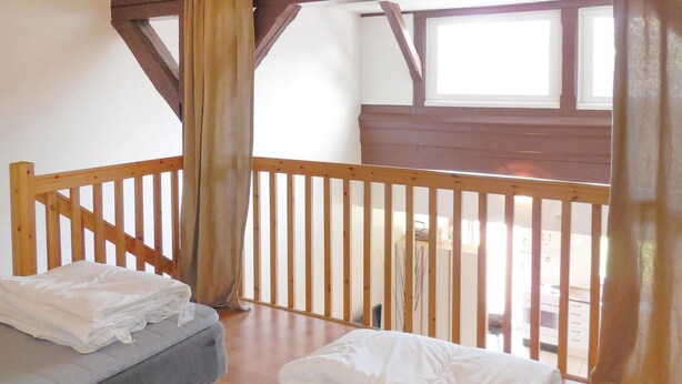 A room with a wooden balcony, a bed with white bedding, and a window with curtains.