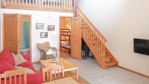 A cozy living room with a red sofa, a wooden table, and a staircase leading to a loft area.