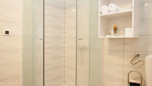 A modern bathroom with a glass shower enclosure, a toilet, and a shelf with towels and toiletries. - Rooms Garden Zagreb Airport (Velika Gorica)
