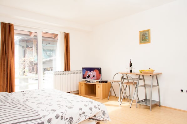 Une chambre à coucher comprenant un lit, une télévision, un bureau avec une chaise, un radiateur et une fenêtre avec des rideaux.