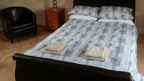 Un dormitorio con cama, una silla, una mesita de noche y una lámpara.