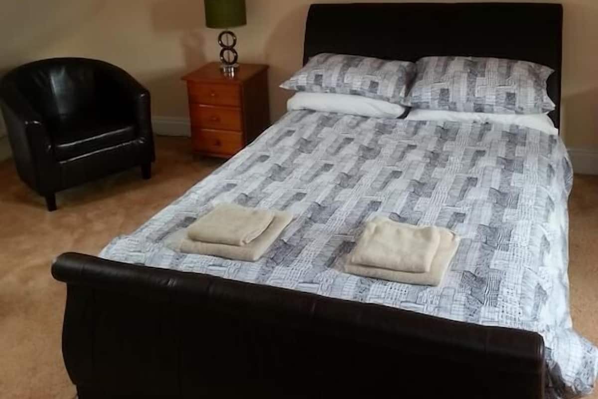 A bedroom with a bed, a chair, a nightstand, and a lamp.
