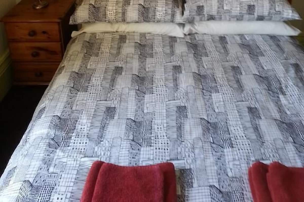 A bed with a patterned bedspread, a wooden headboard, and two pillows.