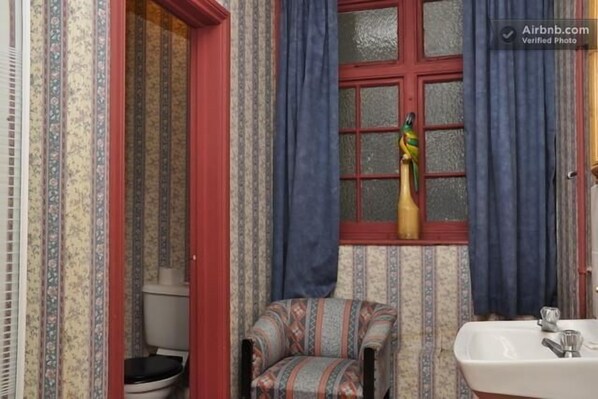 Un baño con inodoro, lavamanos, una silla y un ventanal con cortinas.
